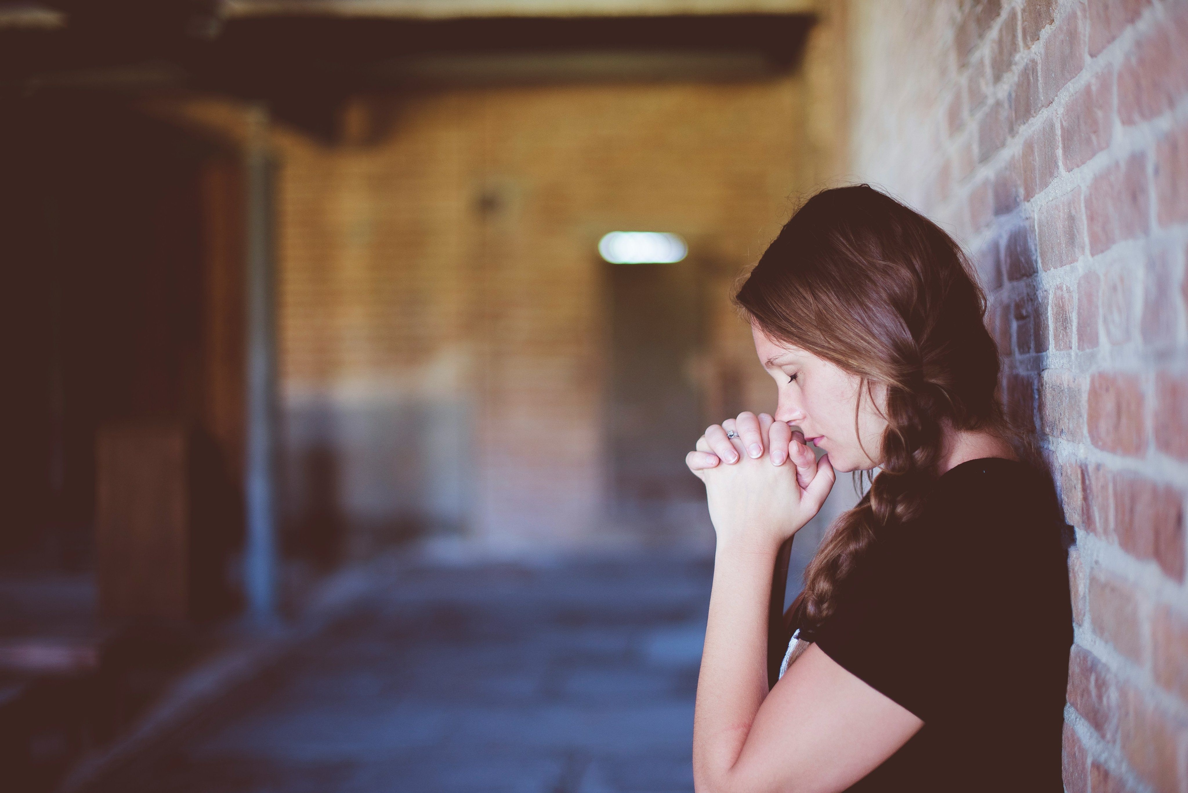 profile of a woman praying back to a wall, hands together, eyes closed